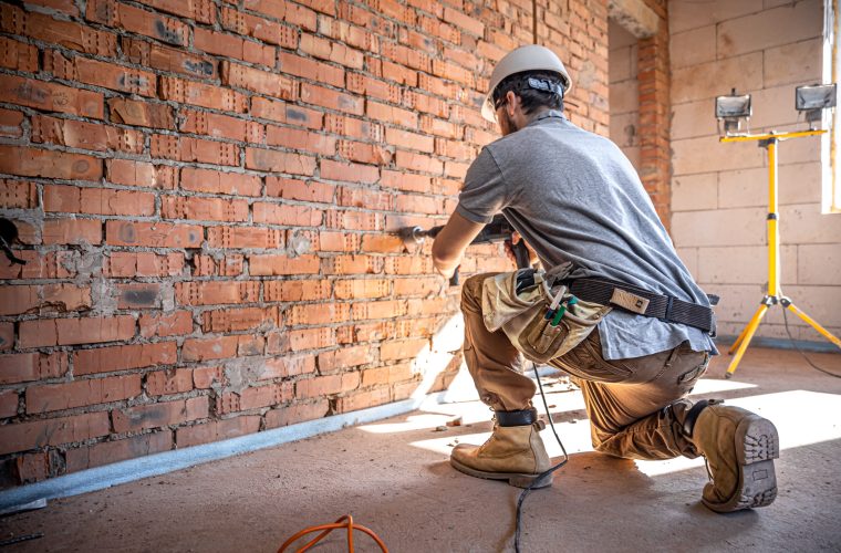 Handyman at a construction site in the process of drilling a wall with a perforator.